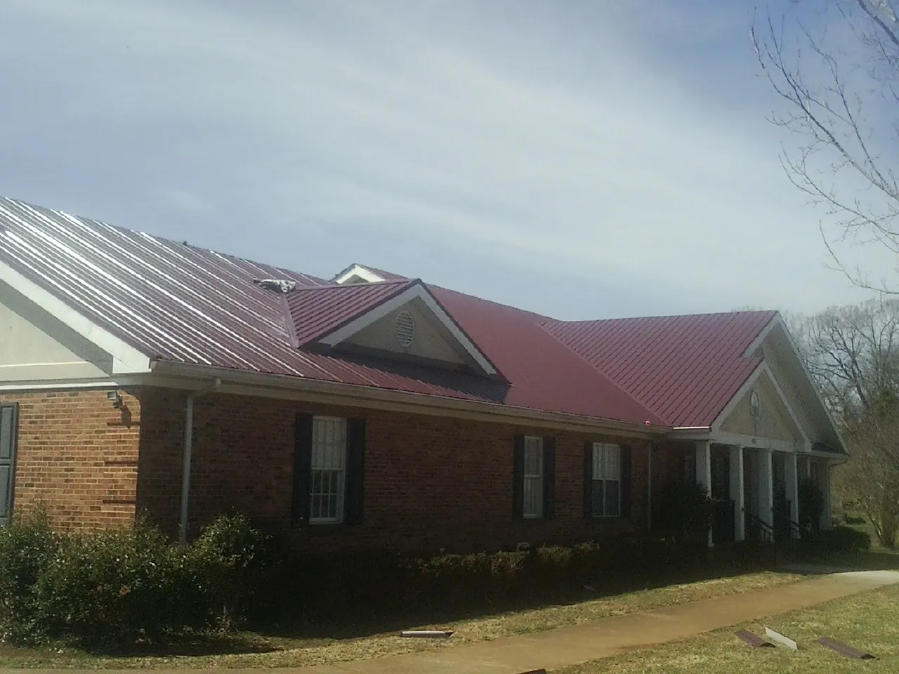Red metal roof with gabled entries on a long brick building, from a Hail Damage Roof Repair job in Tampa