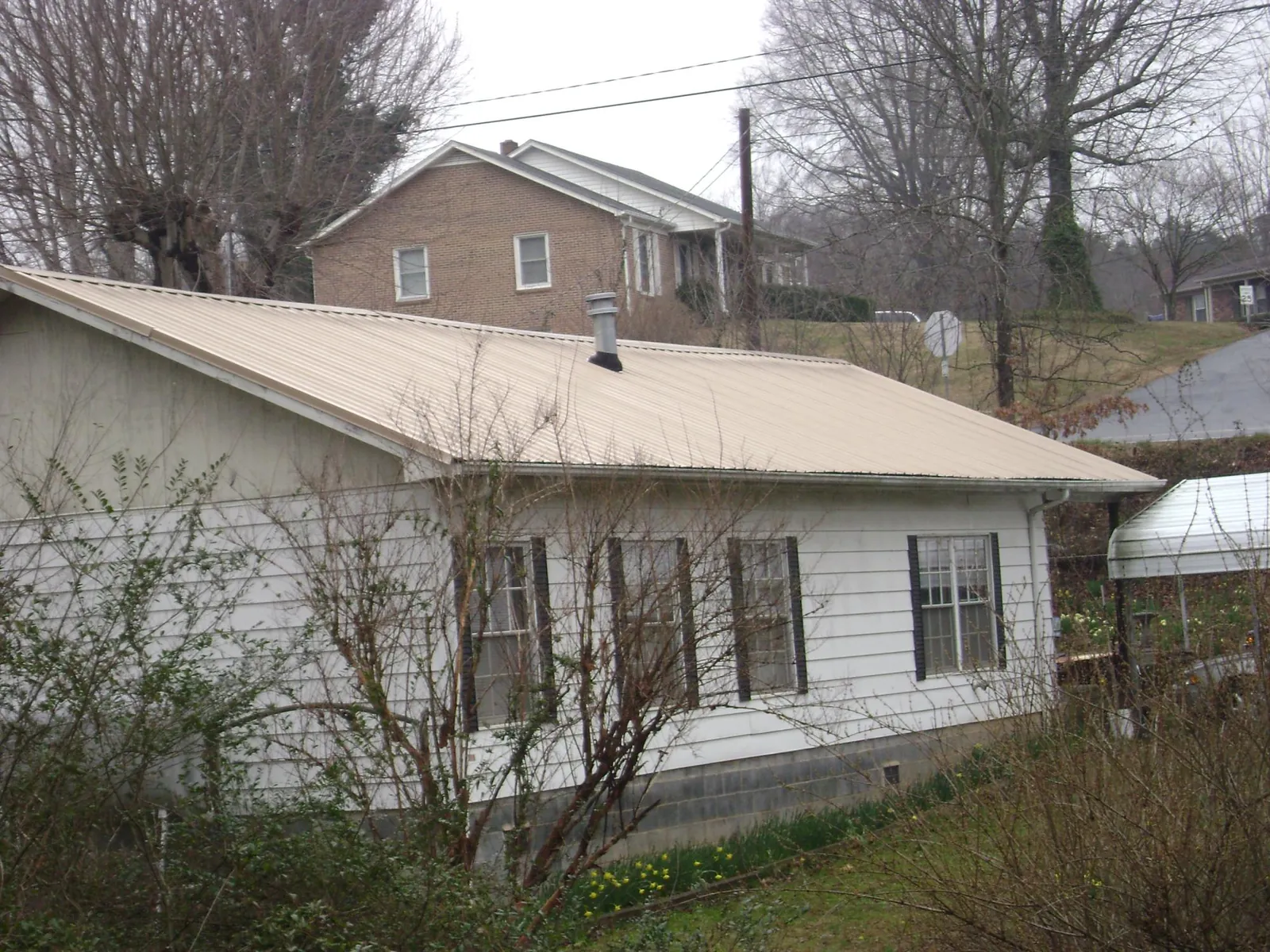 Tan metal roof on a white sided house set into a hillside — Commercial Roofing by Roofing Brothers in Tampa